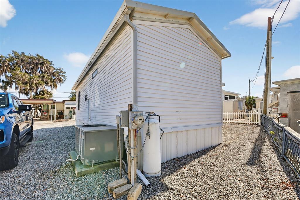 The exterior side of a mobile home features a propane tank, utility meter, and air conditioner — 38237 ORIOLE WAY, LEESBURG, FL