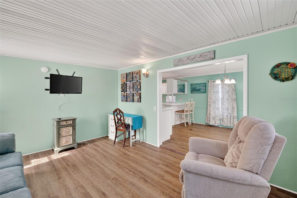 A living room with light green walls, wood-look flooring, and a view into the kitchen — 38237 ORIOLE WAY, LEESBURG, FL
