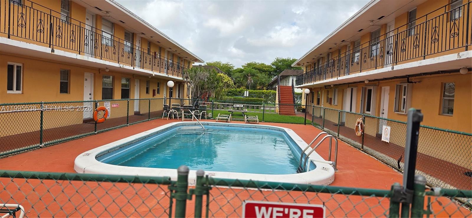 An outdoor swimming pool sits between two yellow two-story apartment buildings with metal railings — 3800 SW 102nd Ave # 108, Miami FL 33165, MIAMI, FL