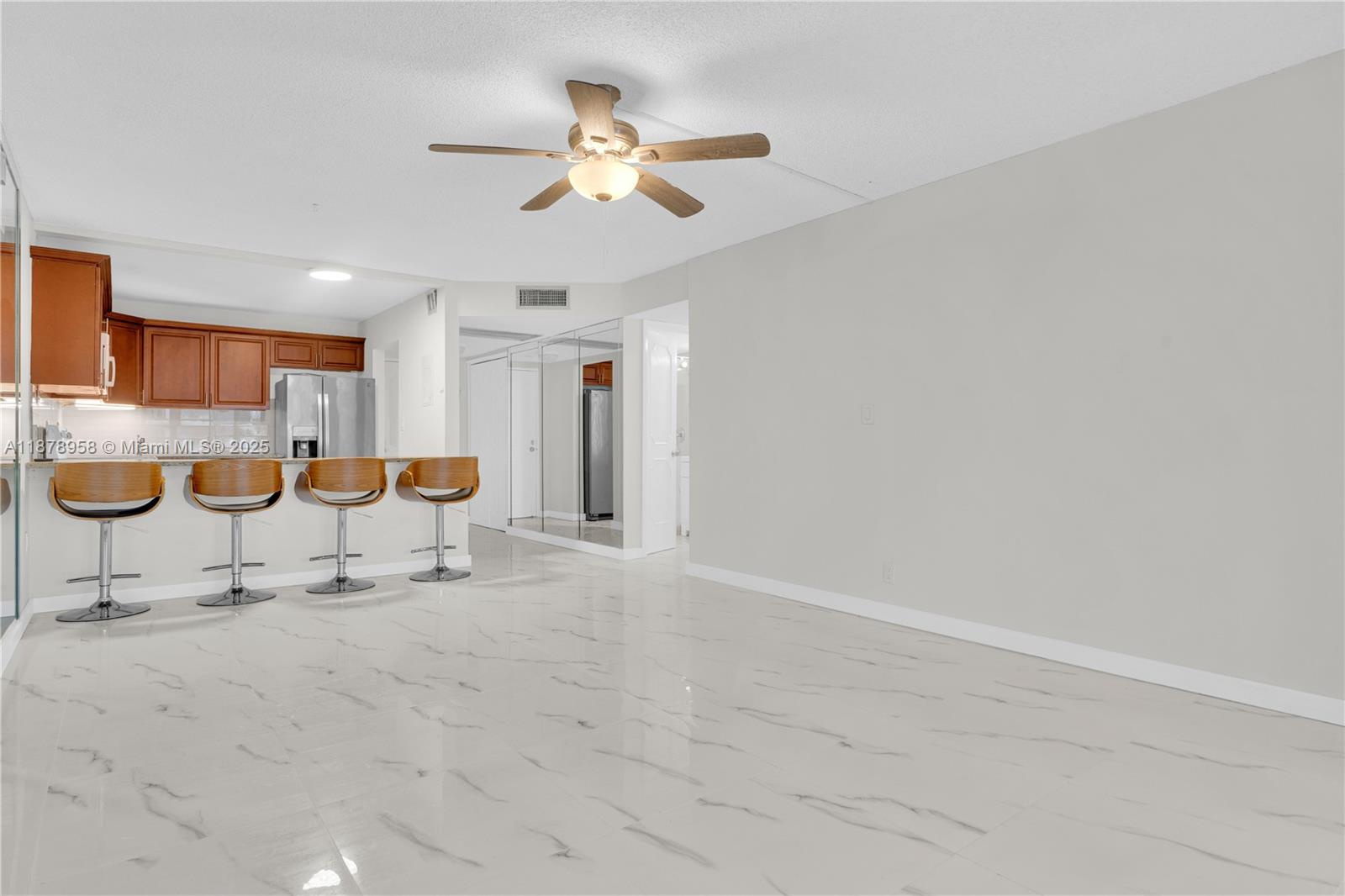 A kitchen with wooden cabinets and a breakfast bar overlooks a spacious, tiled living area — 9355 SW 8th St # 425, Boca Raton FL 33428, BOCA RATON, FL