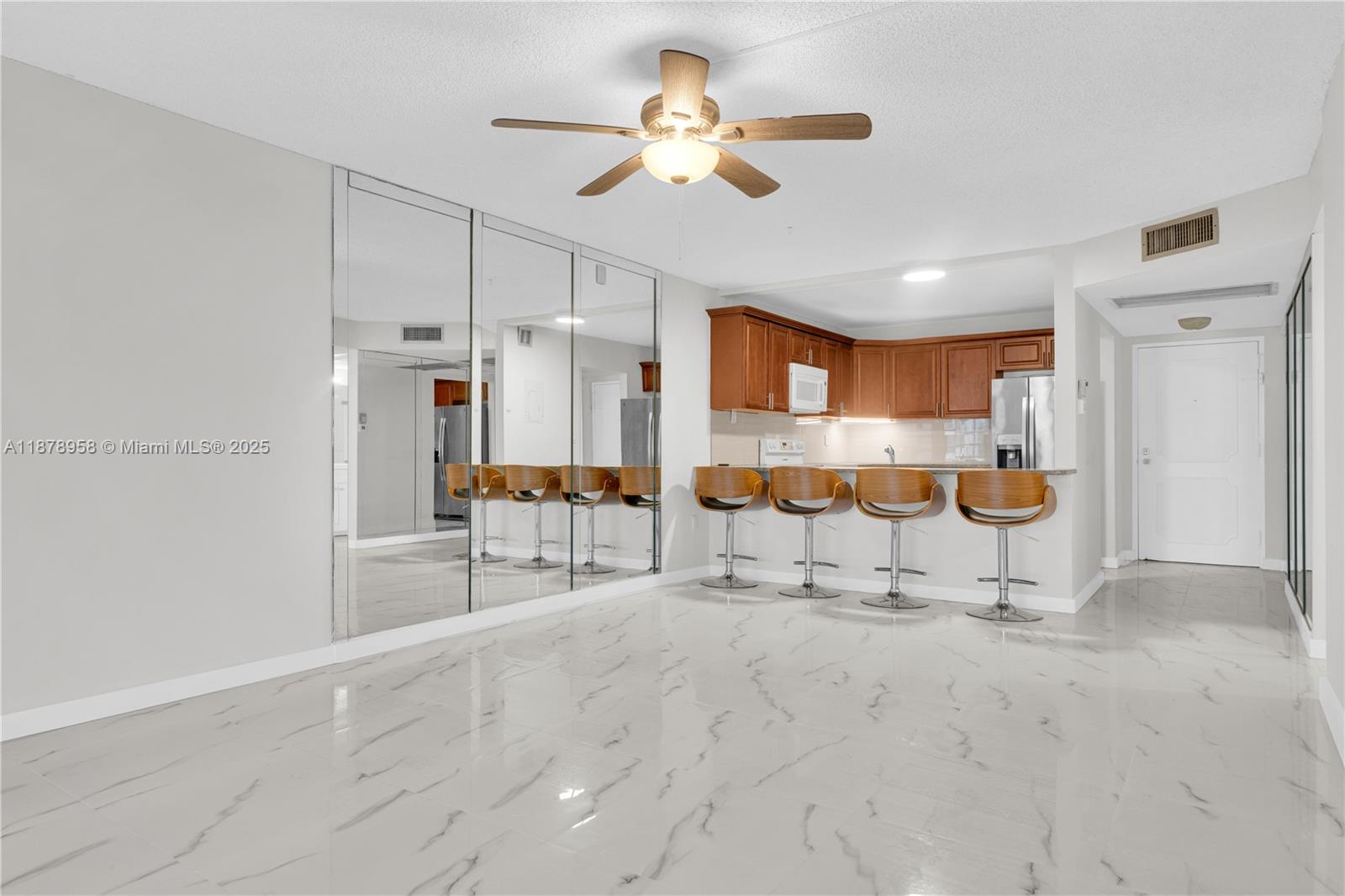 A kitchen with wooden cabinets and a breakfast bar overlooks a room with mirrored walls — 9355 SW 8th St # 425, Boca Raton FL 33428, BOCA RATON, FL