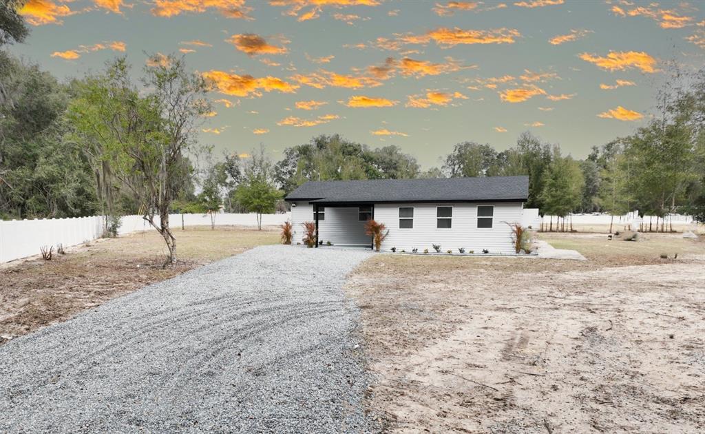 A single-story white house with a black roof sits at the end of a gravel driveway — 2607 NE 140TH STREET, CITRA, FL