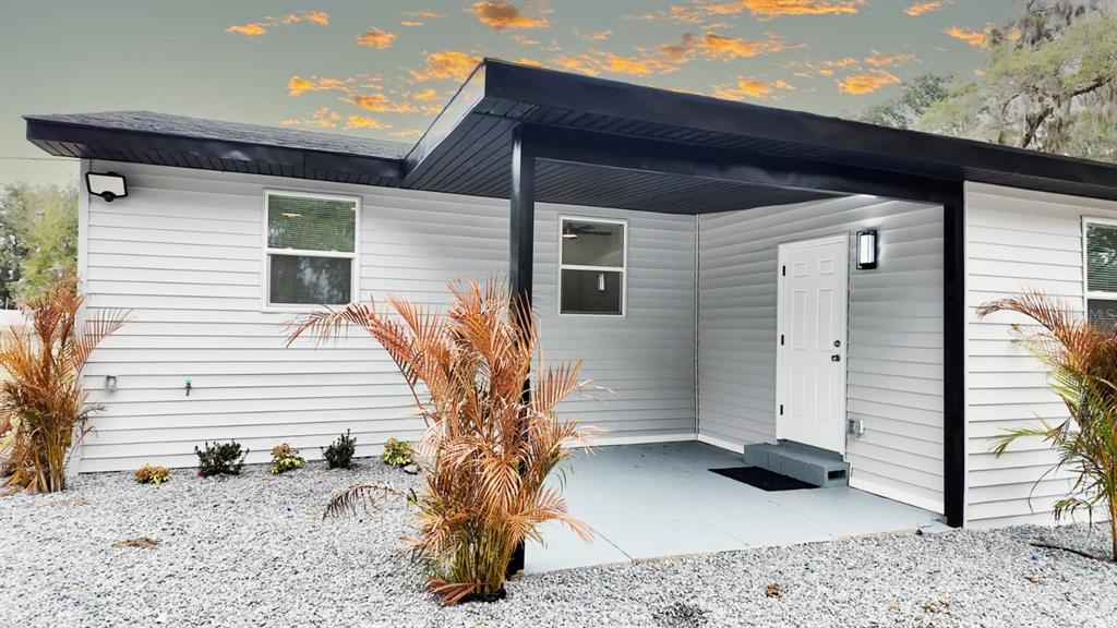 A single-story house exterior with light gray siding, a covered porch, and gravel landscaping — 2607 NE 140TH STREET, CITRA, FL