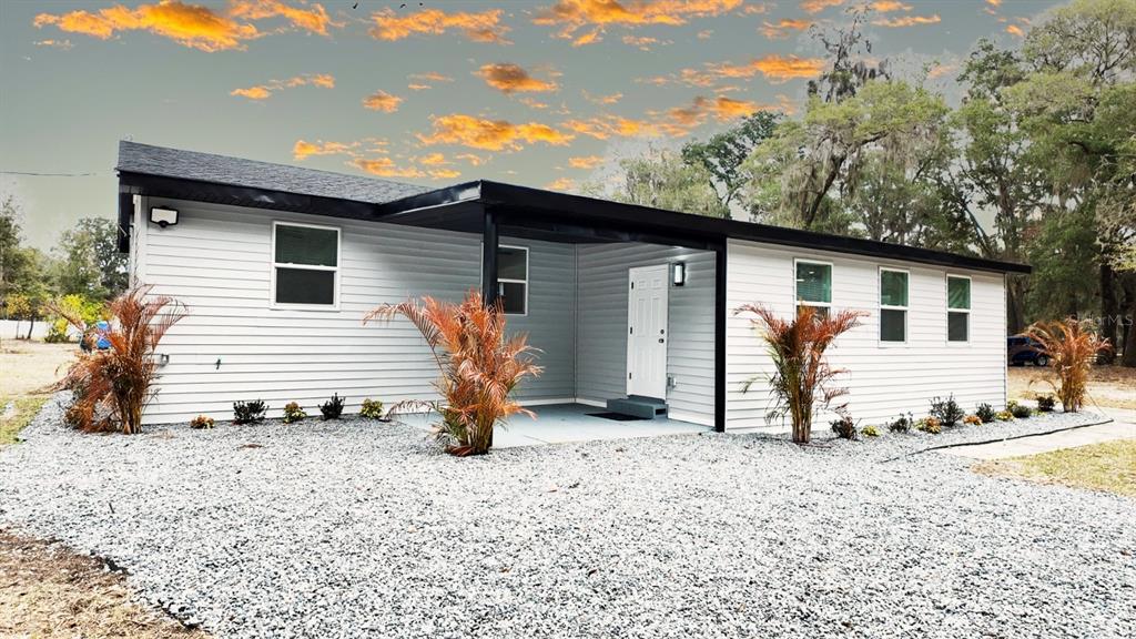 A single-story house with light gray siding and a gravel yard under a sunset sky — 2607 NE 140TH STREET, CITRA, FL