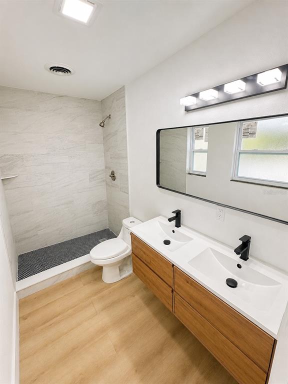 A modern bathroom features a double vanity, a walk-in shower, and light wood-look flooring — 245 16TH STREET NE, WINTER HAVEN, FL