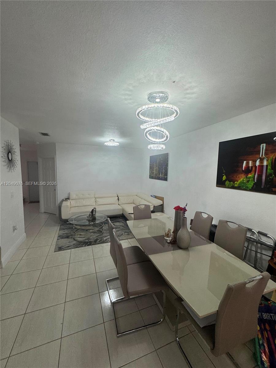 A dining area with a modern chandelier and a sectional sofa in the background — 8743 NW 106th Ln # 8743, Hialeah Gardens FL 33018, HIALEAH GARDENS, FL