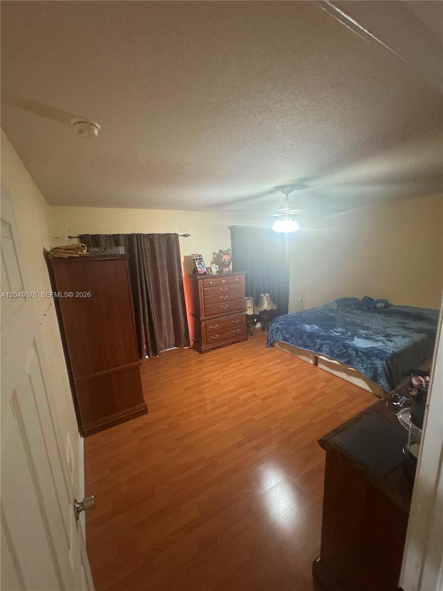 A bedroom features wood-look flooring, a bed with a blue blanket, and wooden furniture — 8743 NW 106th Ln # 8743, Hialeah Gardens FL 33018, HIALEAH GARDENS, FL