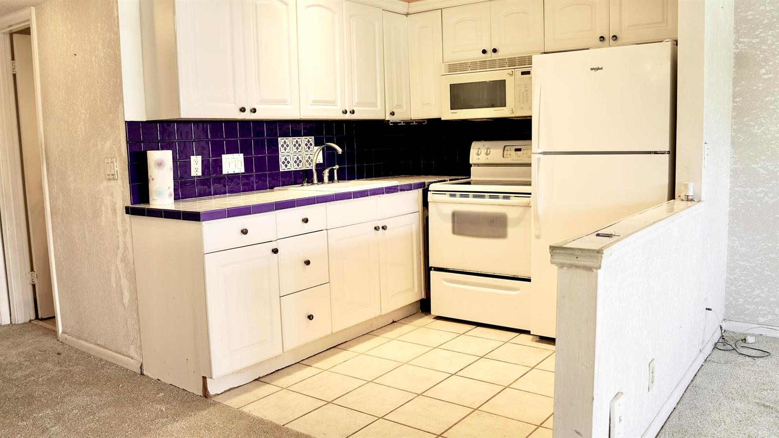 A kitchen with white cabinets, white appliances, and a purple tiled backsplash and countertop — 38 Keswick # B, Deerfield Beach FL 33442, DEERFIELD BEACH, FL