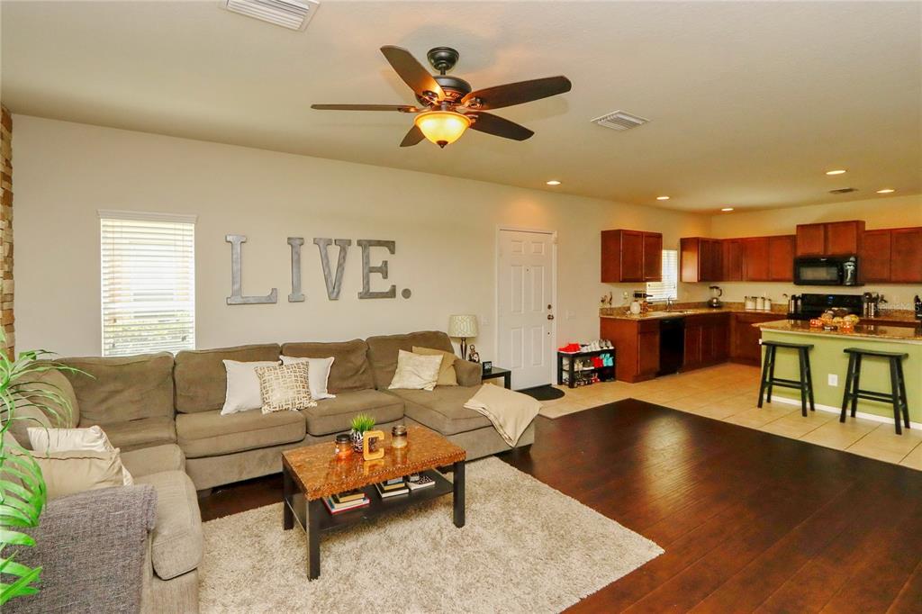 A living room with a sectional sofa and wall lettering opens into a kitchen area — 4724 SOMERSET HILL LANE, RIVERVIEW, FL