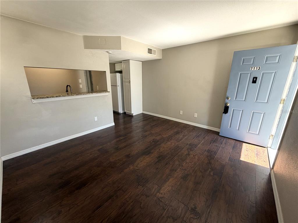 An interior view shows a living area with dark wood flooring, a pass-through window, and a door — 7113 E BANK DRIVE UNIT 7113, TAMPA, FL