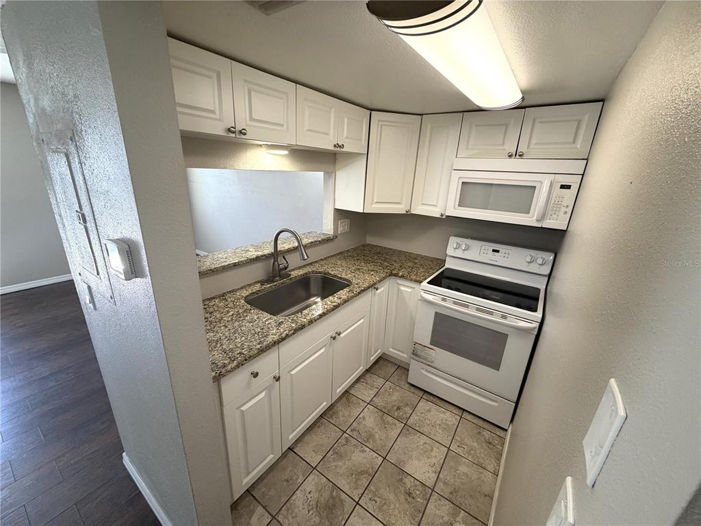 A small kitchen features white cabinets, granite countertops, a white stove, and tile flooring — 7113 E BANK DRIVE UNIT 7113, TAMPA, FL
