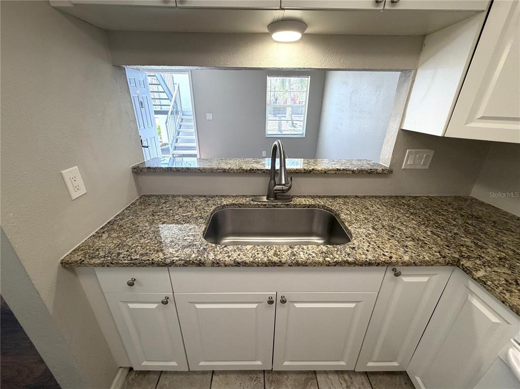 A kitchen sink with granite countertops and white cabinets overlooks an exterior staircase and window — 7113 E BANK DRIVE UNIT 7113, TAMPA, FL