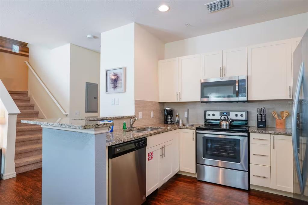 A kitchen with white cabinets, granite countertops, stainless steel appliances, and stairs in the background — 3201 GOLD LANE, KISSIMMEE, FL