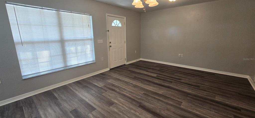 An empty room features gray walls, dark wood-look flooring, a window with blinds, and a door — 2605 NE 22ND AVENUE, OCALA, FL