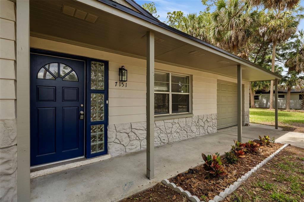 The exterior of a house features a blue front door, glass blocks, and stone siding — 7151 PINEWOOD DRIVE, NEW PORT RICHEY, FL