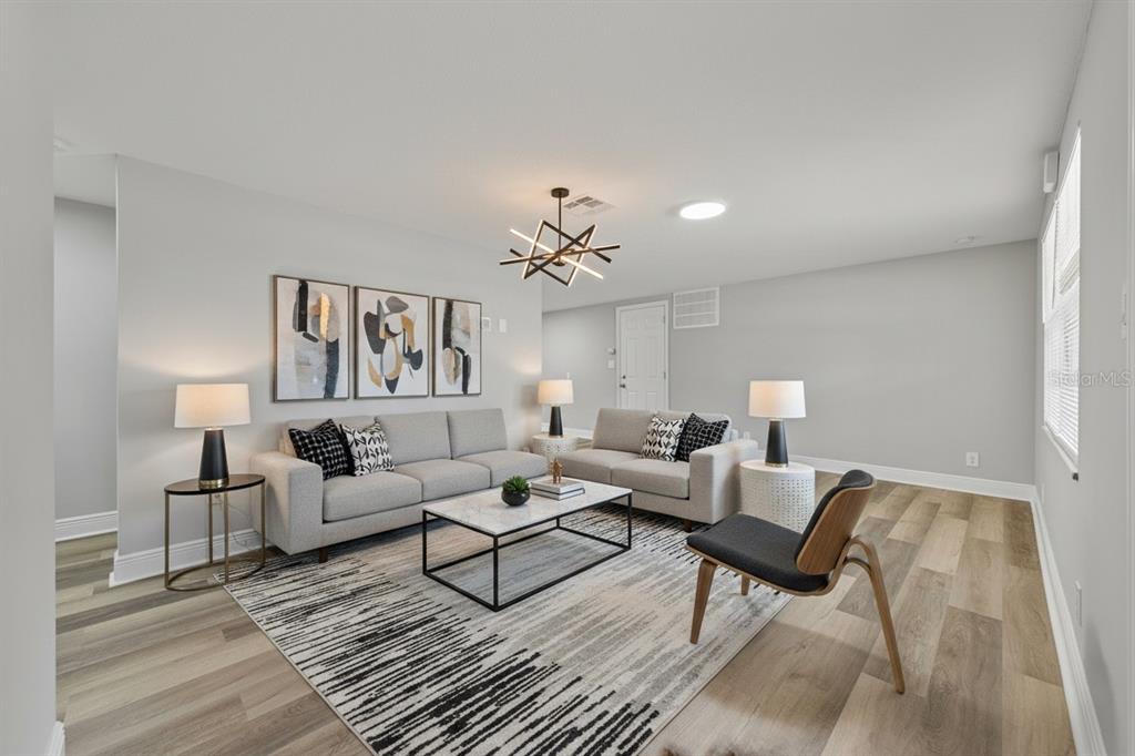 A modern living room features gray sofas, a geometric chandelier, and wood-look vinyl flooring — 7151 PINEWOOD DRIVE, NEW PORT RICHEY, FL