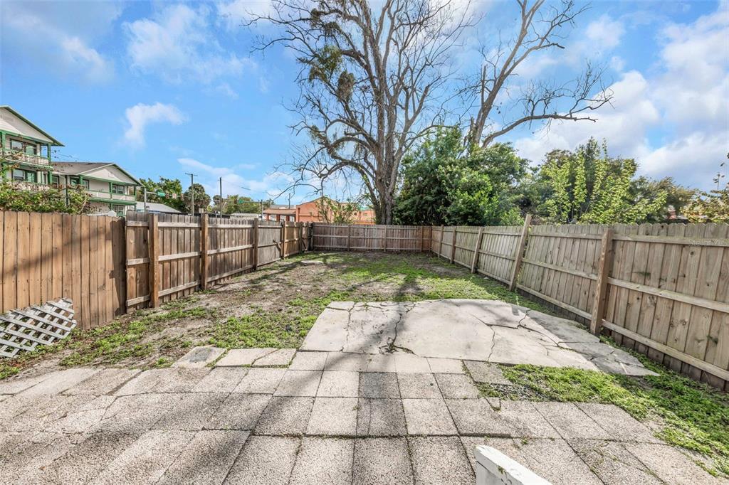 A fenced backyard features a cracked concrete patio and a large tree under a blue sky — 2613 N 21ST STREET, TAMPA, FL