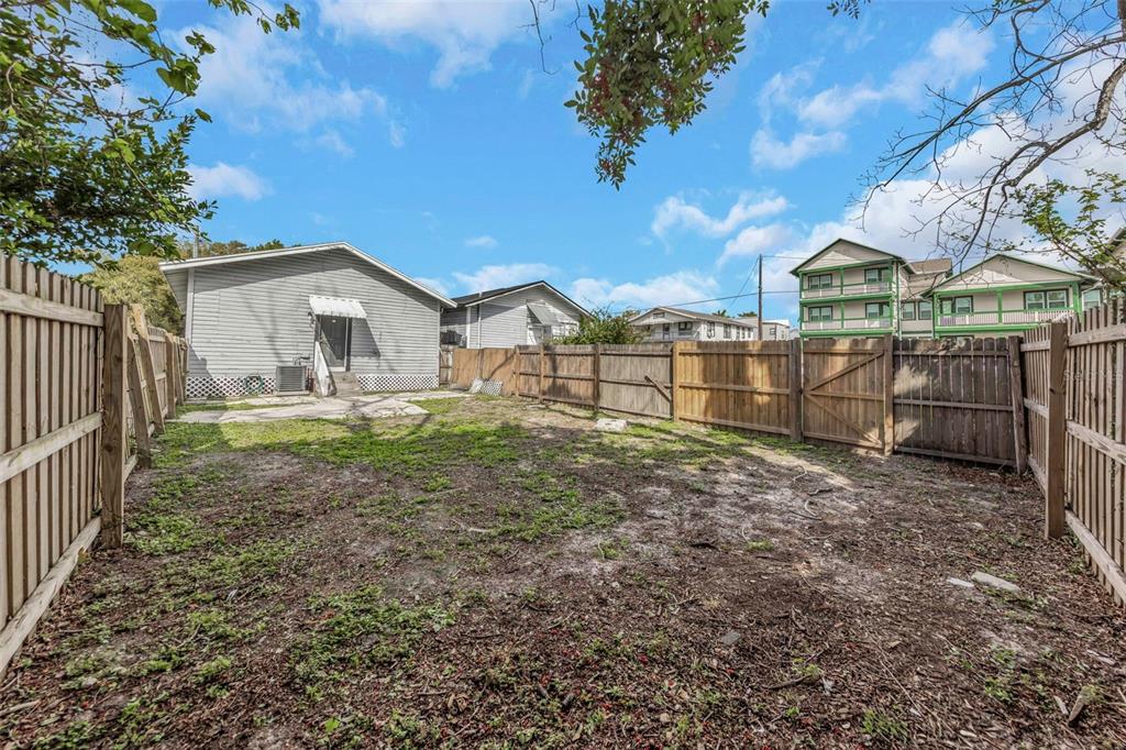 A fenced backyard with sparse grass and a gray house in the background — 2613 N 21ST STREET, TAMPA, FL