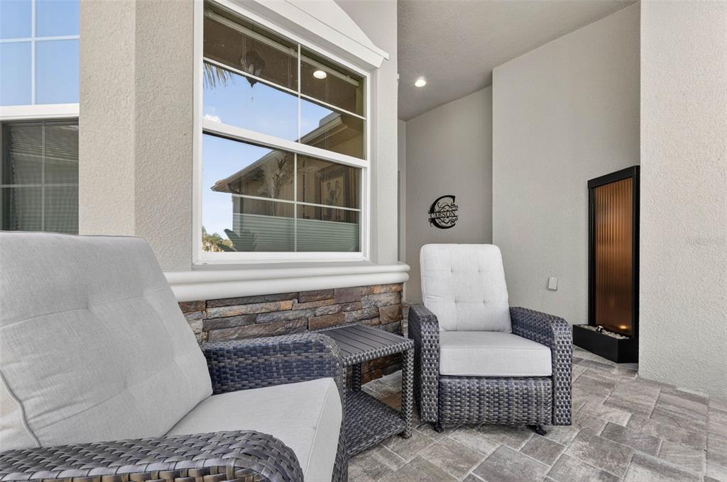 A covered patio features two wicker chairs, a small table, and a wall-mounted water feature — 30724 LINDENTREE DRIVE, WESLEY CHAPEL, FL
