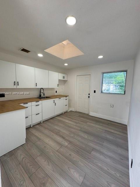 A kitchen features white cabinets, wood-look flooring, a skylight, and a door to the outside — 26 Virginia Rd, West Park FL 33023, WEST PARK, FL