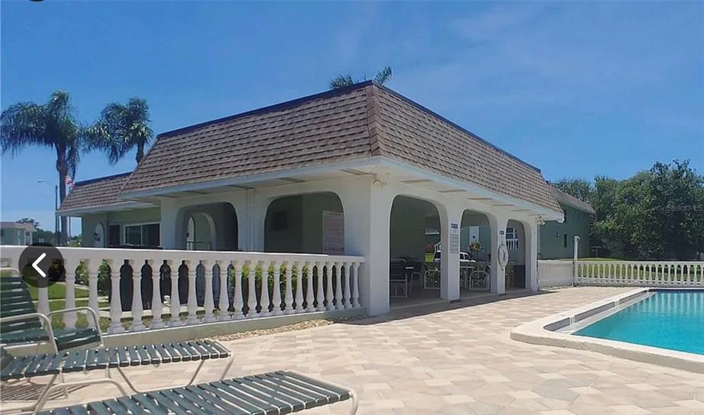 A covered outdoor patio with arched openings sits beside a swimming pool and lounge chairs — 1250 S PINELLAS AVENUE UNIT 306, TARPON SPRINGS, FL