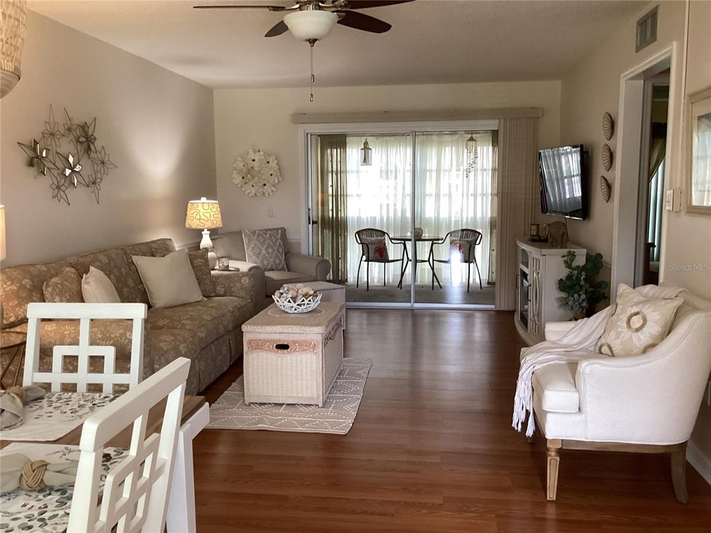 A living room features wood-look flooring, a patterned sofa, a white armchair, and sliding doors — 1250 S PINELLAS AVENUE UNIT 306, TARPON SPRINGS, FL