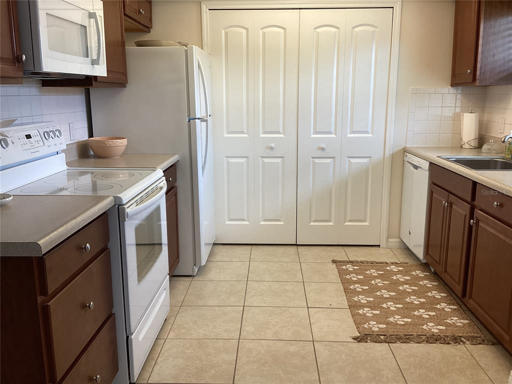 A kitchen features wooden cabinets, white appliances, tile flooring, and a double-door pantry closet — 1250 S PINELLAS AVENUE UNIT 306, TARPON SPRINGS, FL