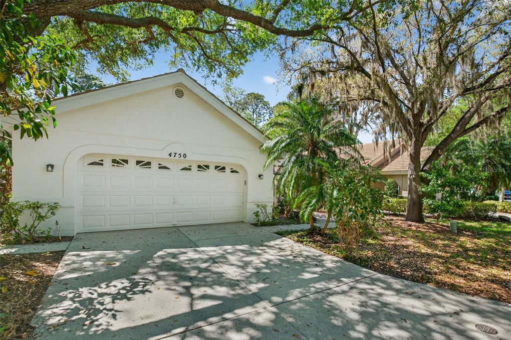 A white house exterior features a two-car garage with a concrete driveway and mature trees — 4750 TIVOLI AVENUE, SARASOTA, FL