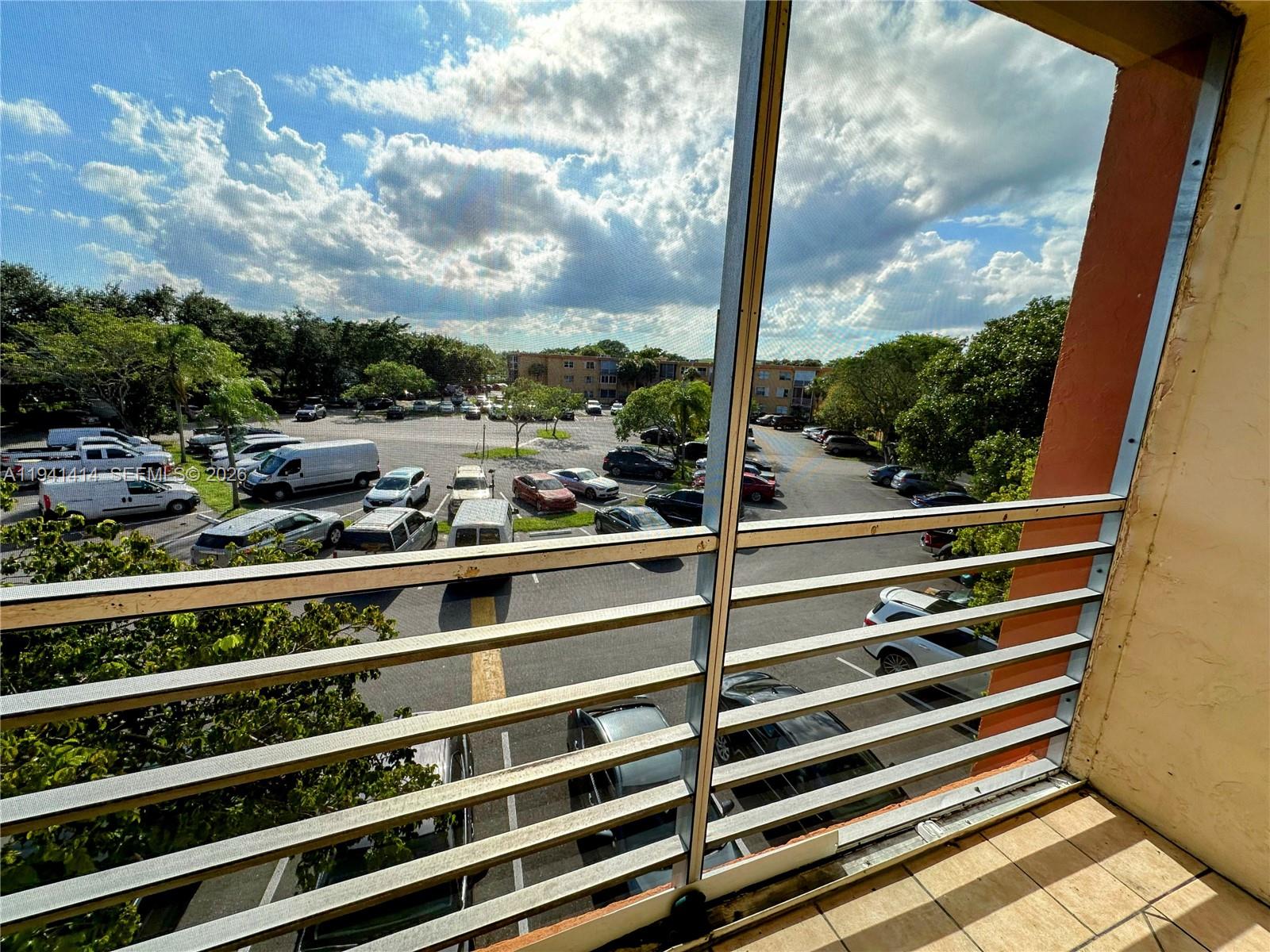 A balcony with metal railings overlooks a parking lot filled with various cars — 4364 NW 9th Ave # 3F, Deerfield Beach FL 33064, DEERFIELD BEACH, FL