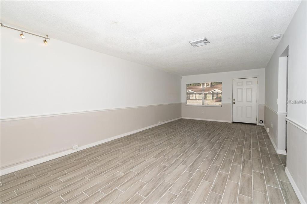 An empty room features light gray wood-look tile flooring, white walls with wainscoting, and track lighting — 1267 WOODMAN WAY, ORLANDO, FL