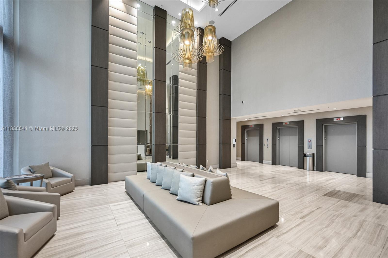A modern building lobby features a large sofa, three elevators, and decorative gold pendant lights — 1010 SW 2nd Avenue # 1107, Miami FL 33130, MIAMI, FL