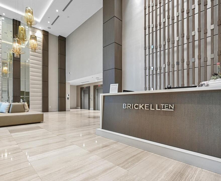 A modern lobby features a reception desk, marble floors, tall columns, and decorative gold pendant lights — 1010 SW 2nd Avenue # 1107, Miami FL 33130, MIAMI, FL
