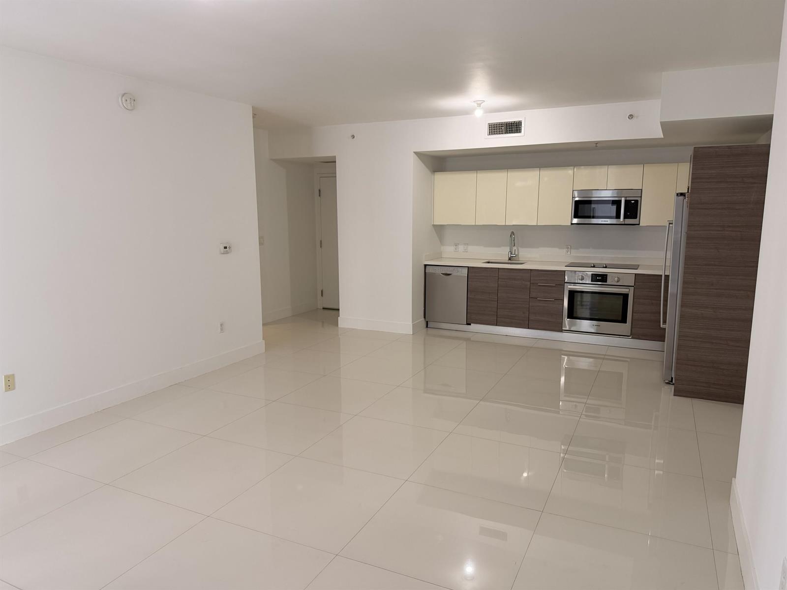 An open-concept kitchen with two-tone cabinetry and stainless steel appliances overlooks a tiled living area — 1010 SW 2nd Avenue # 1107, Miami FL 33130, MIAMI, FL