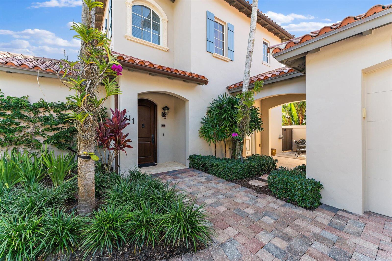 A paved walkway leads to the arched front entrance of a stucco house with tile roofing — 611 White Pelican Way, Jupiter FL 33477, JUPITER, FL