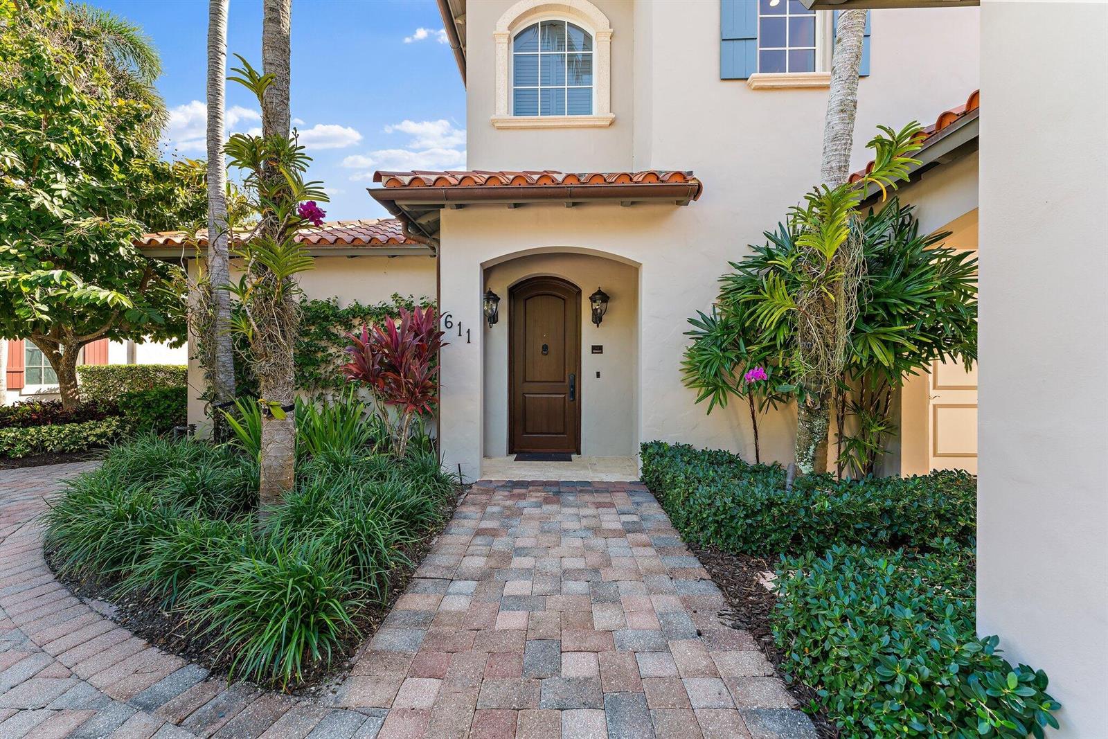 A paved walkway leads to the arched wooden front door of a stucco house — 611 White Pelican Way, Jupiter FL 33477, JUPITER, FL