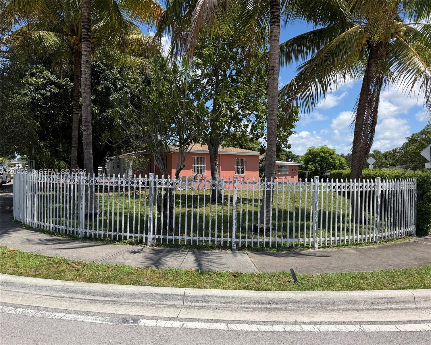 A peach-colored house sits behind a white metal fence surrounded by palm trees — MIAMI, FL