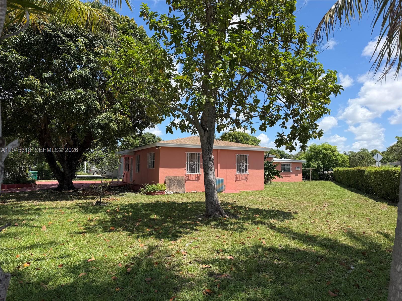 A peach-colored house with security bars on the windows sits on a grassy lot — MIAMI, FL