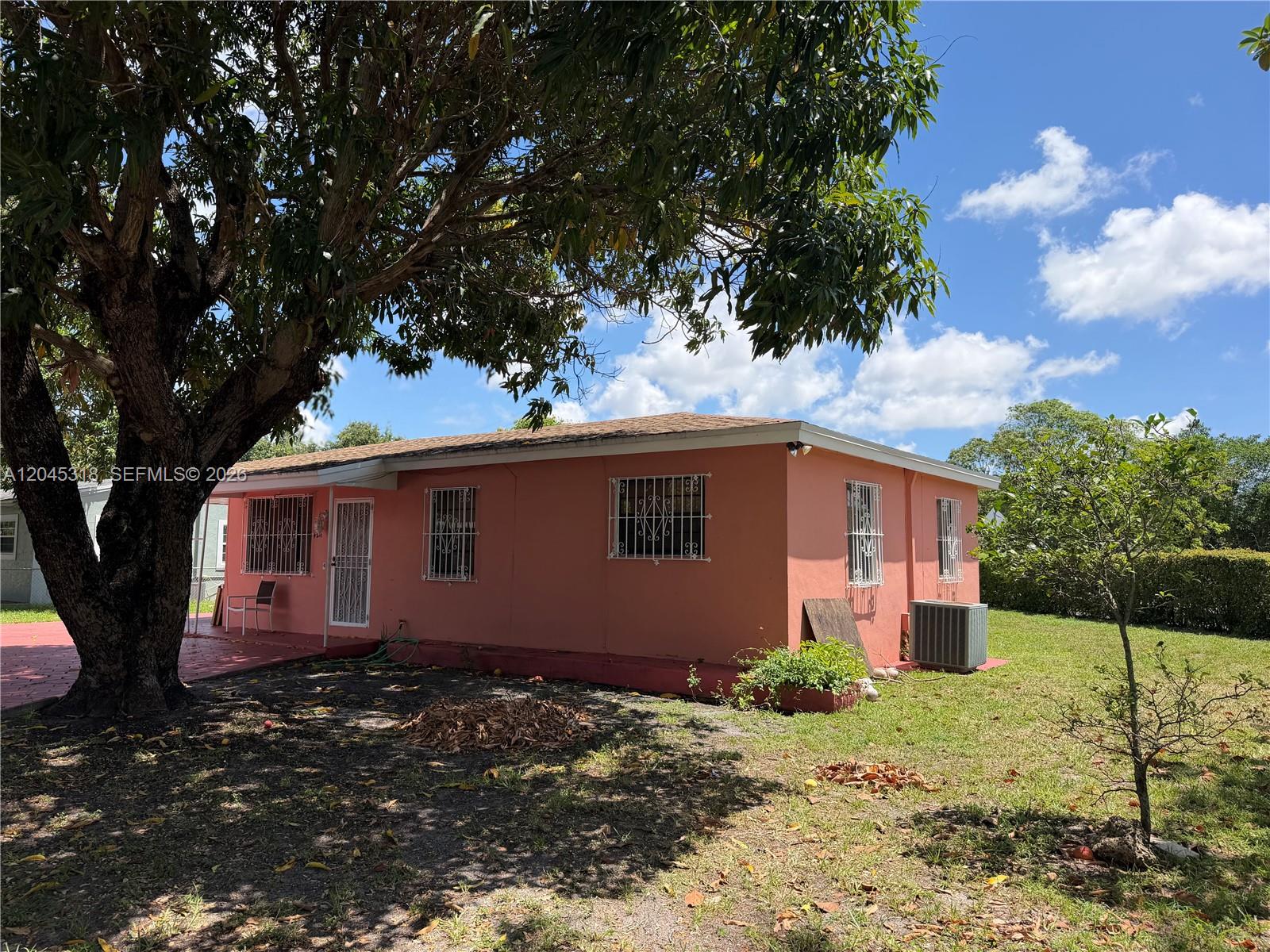 A peach-colored single-story house with security bars on the windows sits under a large tree — MIAMI, FL