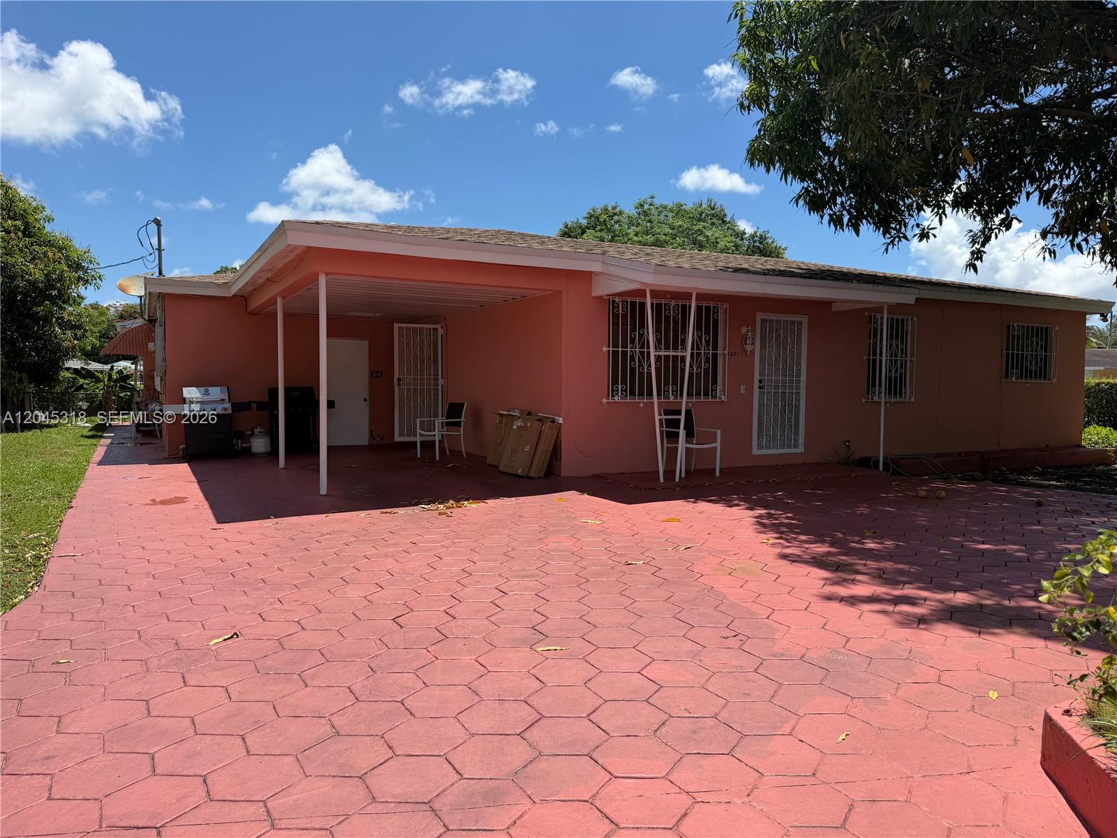A pink, single-story house features a covered carport and a red patterned concrete driveway — MIAMI, FL