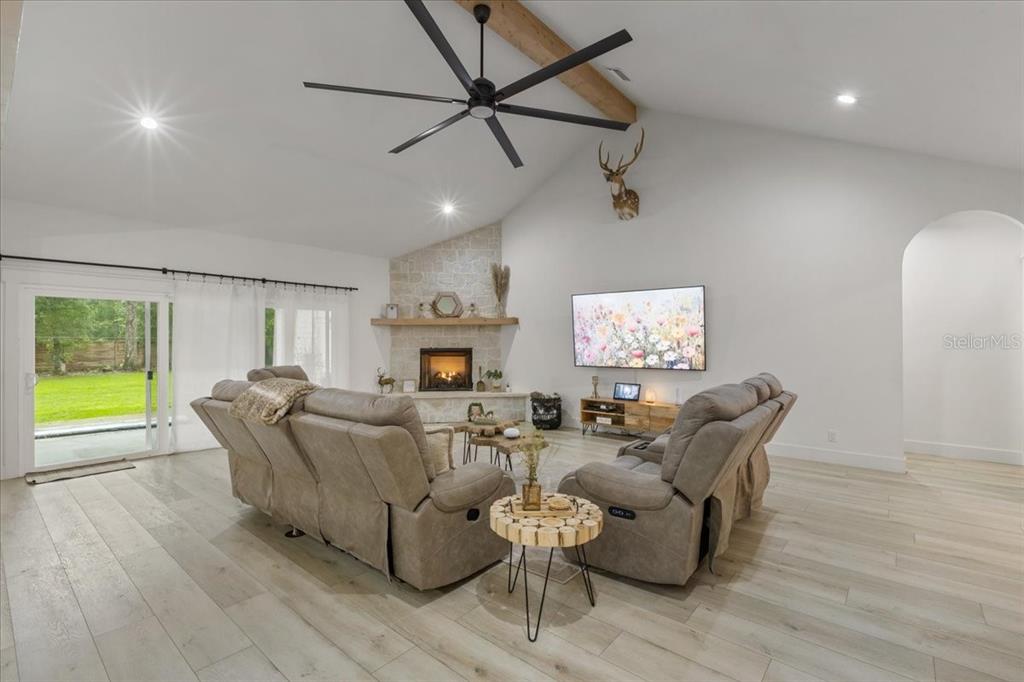 A living room features a stone fireplace, vaulted ceiling, wood-look flooring, and two reclining sofas — 9061 KATHERINE WAY, FANNING SPRINGS, FL