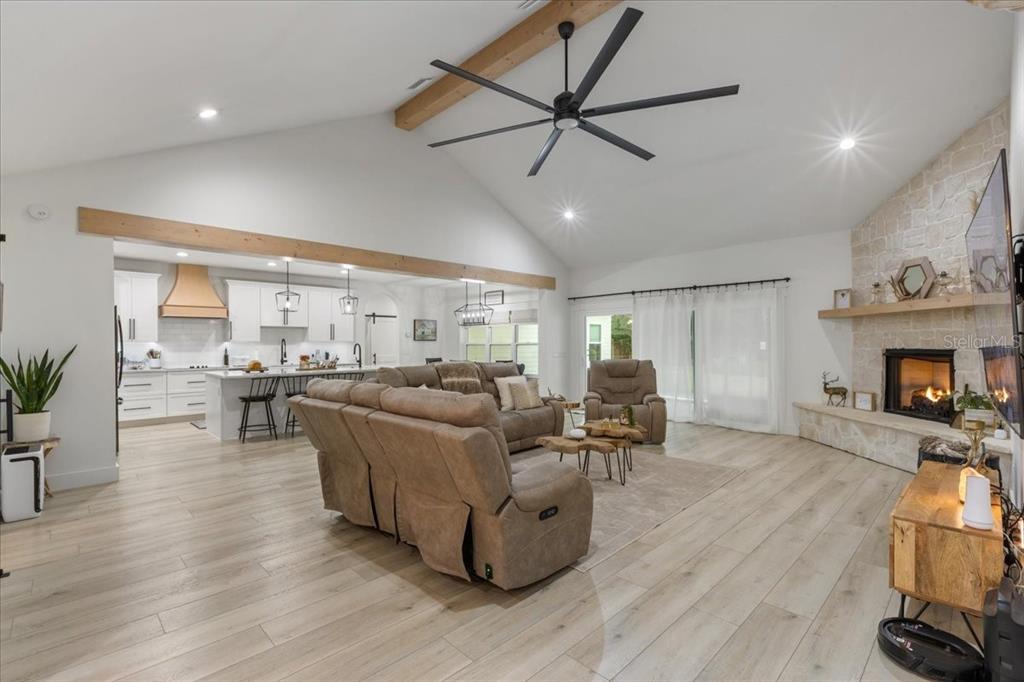 A spacious open-concept living room features a vaulted ceiling, stone fireplace, and light wood flooring — 9061 KATHERINE WAY, FANNING SPRINGS, FL