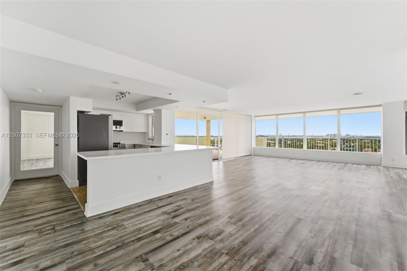 An open-concept kitchen and living area features light wood-look flooring and floor-to-ceiling windows — 2000 NE 135th St PH, North Miami FL 33181, NORTH MIAMI, FL