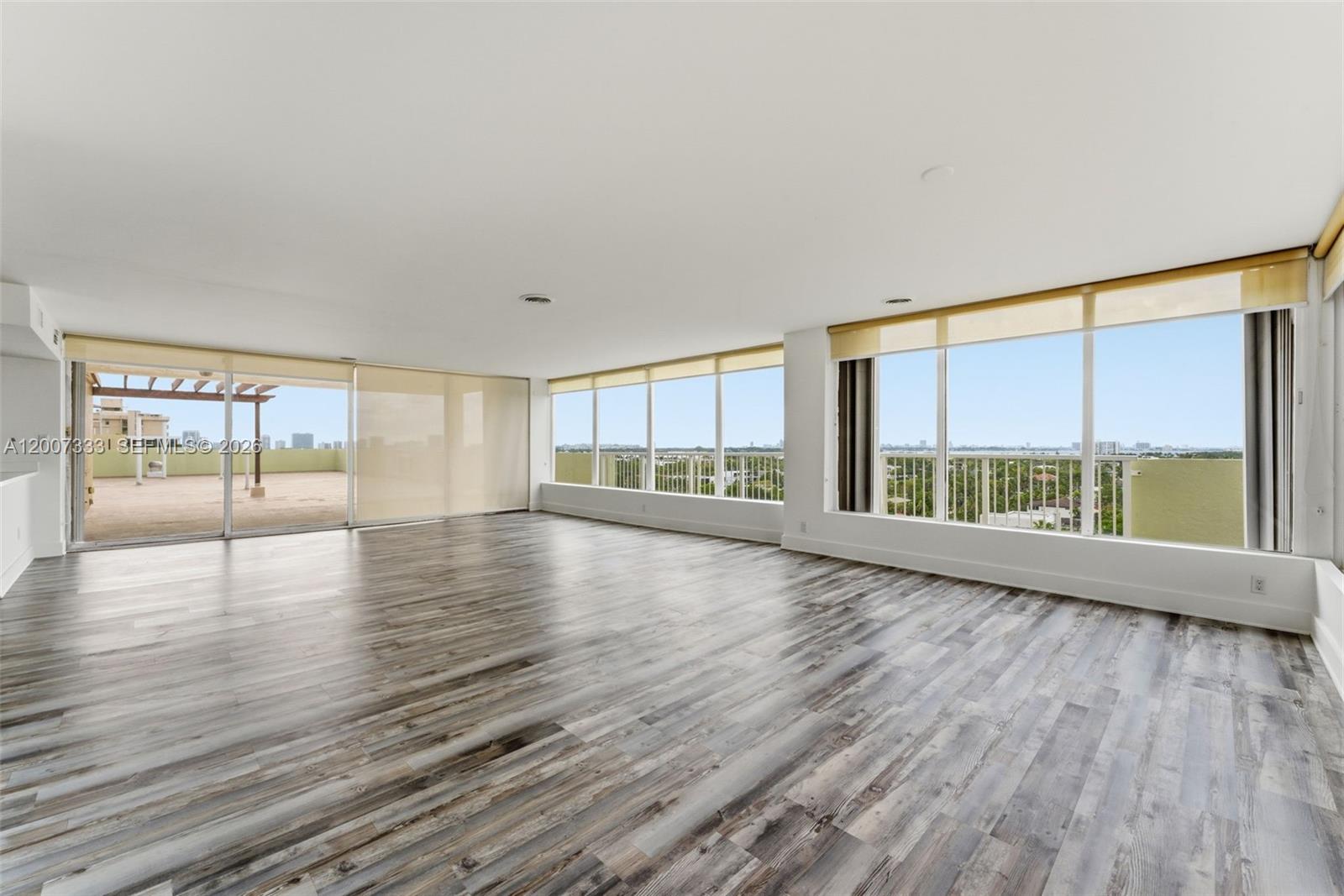 An empty room features wood-look flooring, white walls, large windows, and a sliding glass door — 2000 NE 135th St PH, North Miami FL 33181, NORTH MIAMI, FL