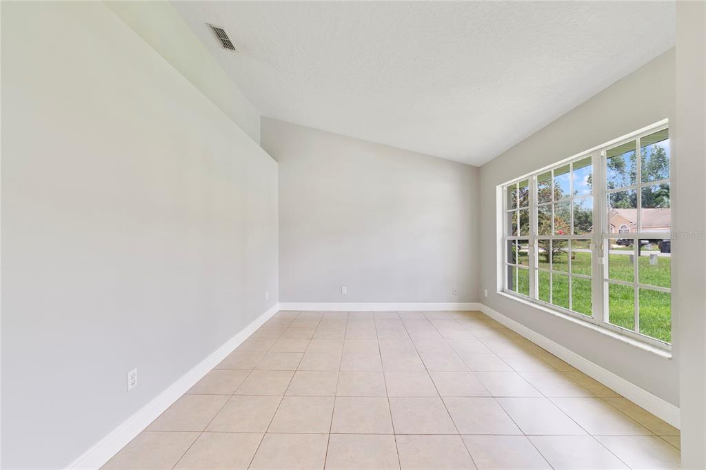 An empty room with light-colored tile flooring, vaulted ceilings, and a large grid-pane window — 309 WILD FORREST DRIVE, DAVENPORT, FL