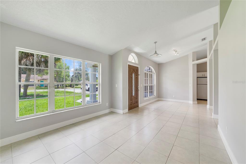A bright, tiled living room features a wooden front door, large windows, and vaulted ceilings — 309 WILD FORREST DRIVE, DAVENPORT, FL