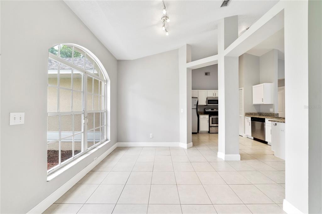 A bright dining area with light tile flooring, a large arched window, and a kitchen view — 309 WILD FORREST DRIVE, DAVENPORT, FL