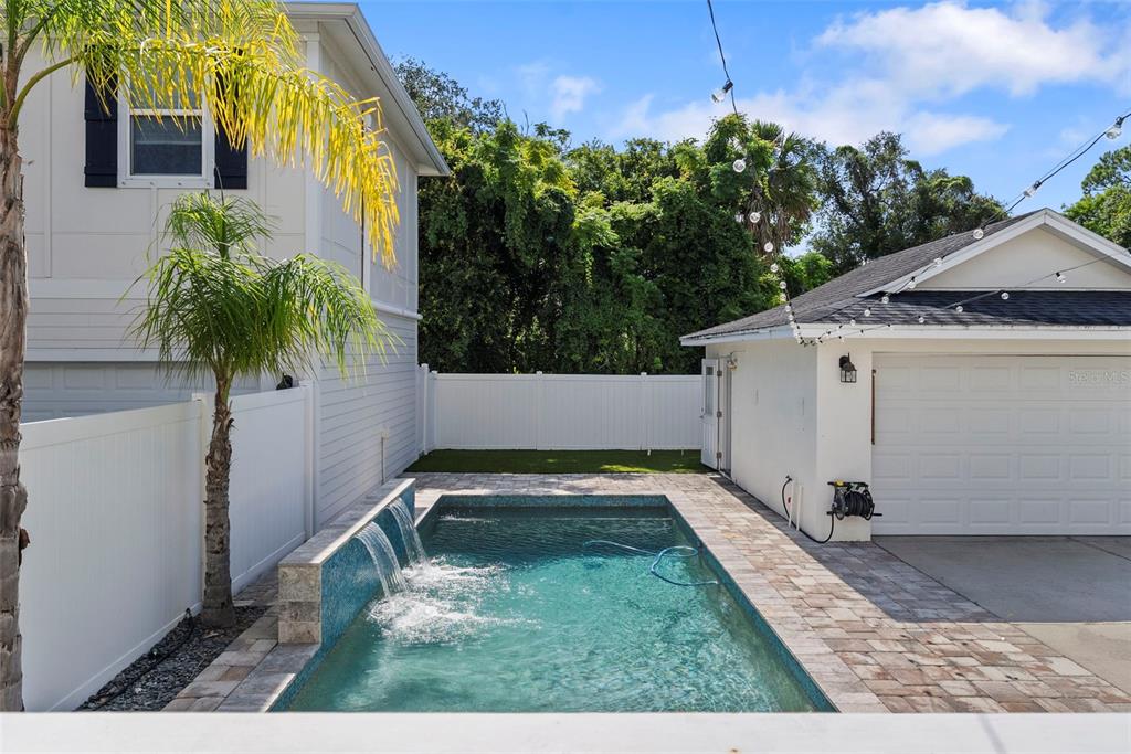 A small rectangular swimming pool with a waterfall feature sits between a house and garage — 11213 MOULTRIE PLACE, TAMPA, FL