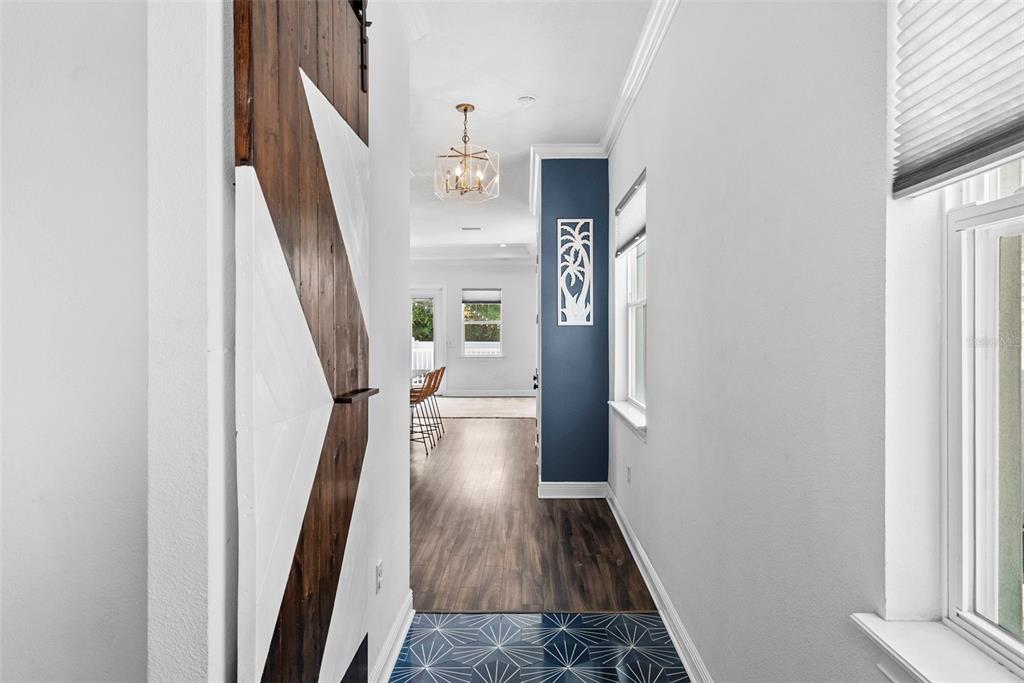 A hallway with patterned tile flooring leads toward a kitchen with a wooden barn door — 11213 MOULTRIE PLACE, TAMPA, FL