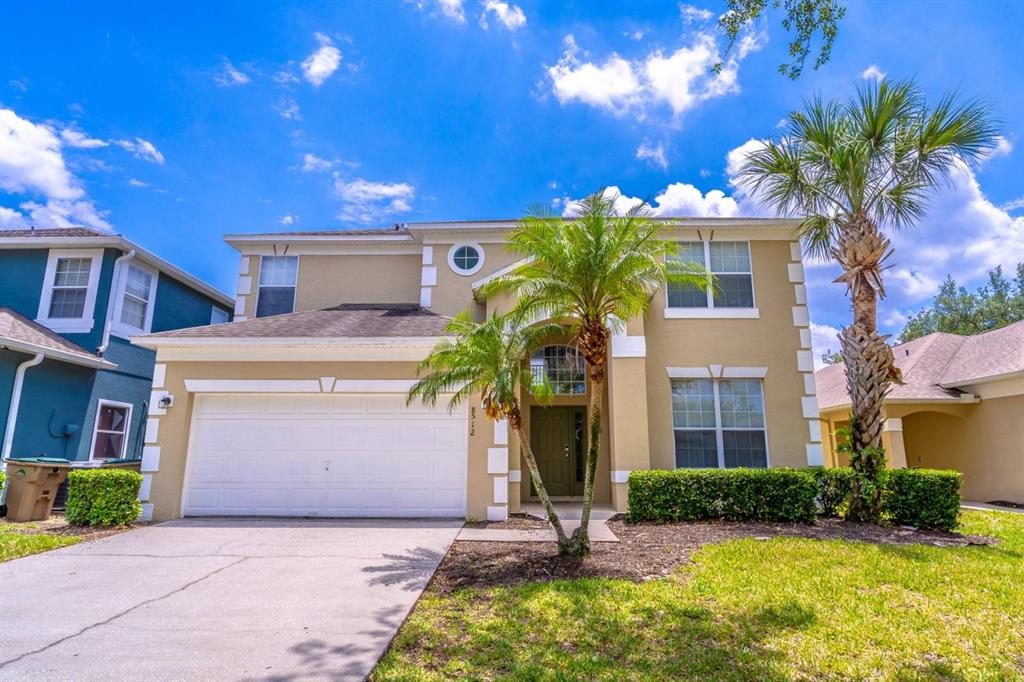 A two-story suburban house with a tan stucco exterior, a two-car garage, and palm trees — 8512 SUNRISE KEY DRIVE, KISSIMMEE, FL