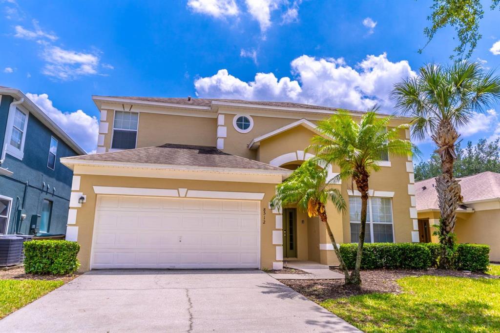A two-story tan house with a white garage door and a palm tree in front — 8512 SUNRISE KEY DRIVE, KISSIMMEE, FL